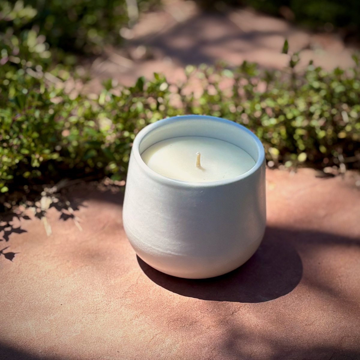White organic ceramic candle on a stone surface with greenery in the background, branded 'The Organic Candle Co'.
