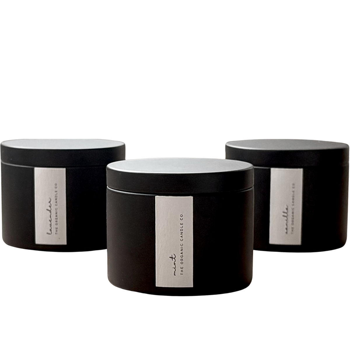 Three organic candles in black cylindrical containers with white labels on a neutral background