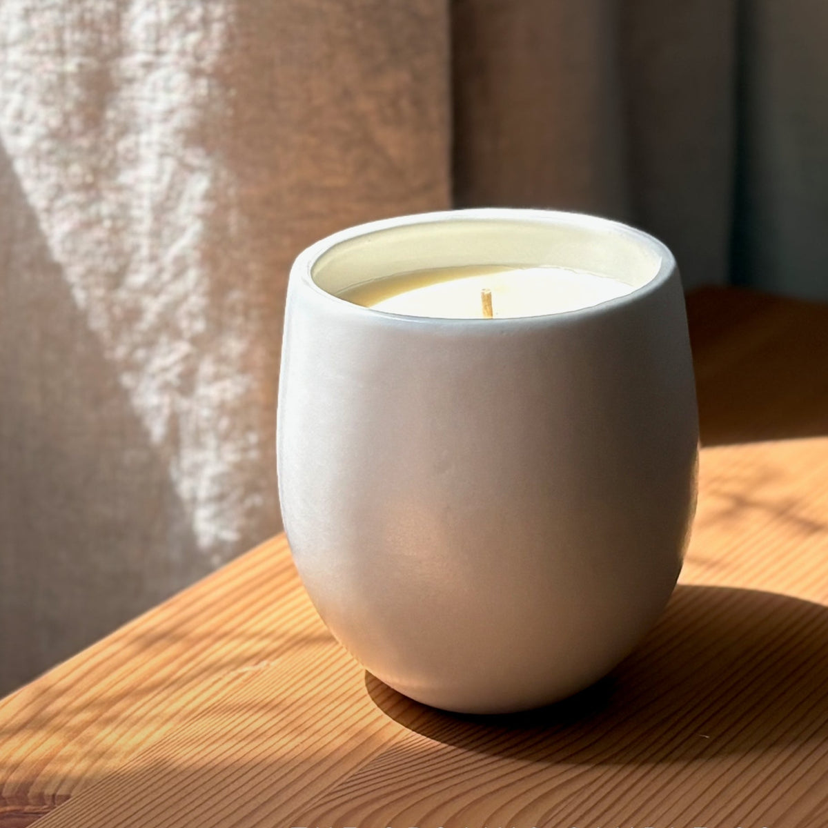 White organic candle in a ceramic vessel on a wooden surface with 'The Organic Candle Co.' branding.
