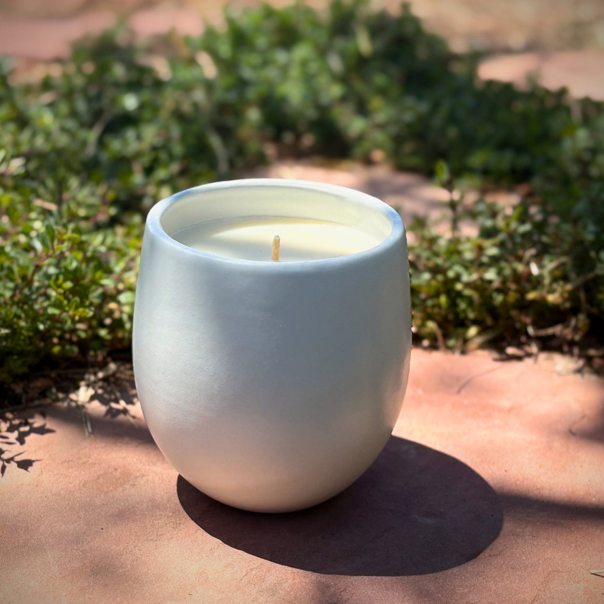 White organic candle in a ceramic vessel on a stone surface with greenery in the background, featuring 'The Organic Candle Co.'