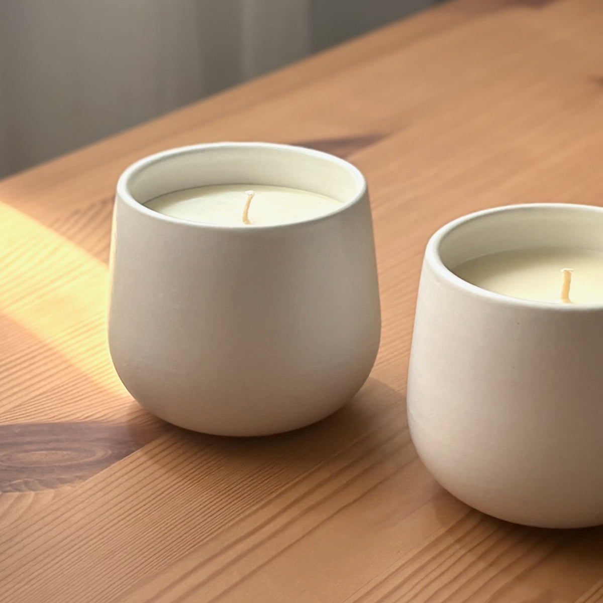 Two white organic candles on a wooden surface with 'The Organic Candle Co.' brand