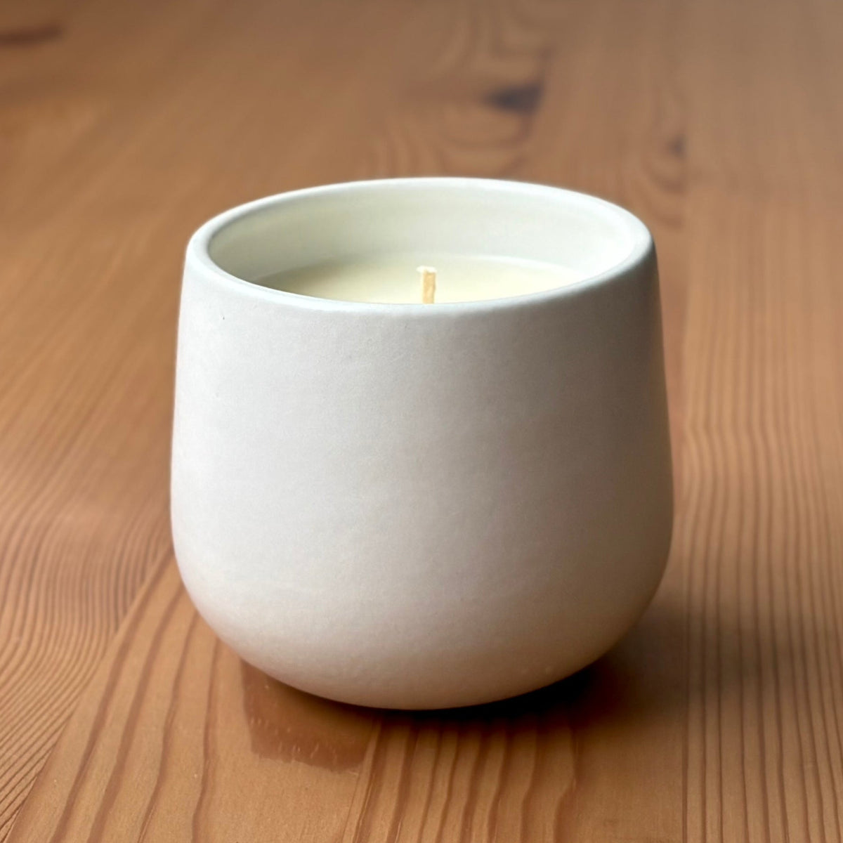 White organic candle in a ceramic holder on a wooden surface with 'The Organic Candle Co.' branding.