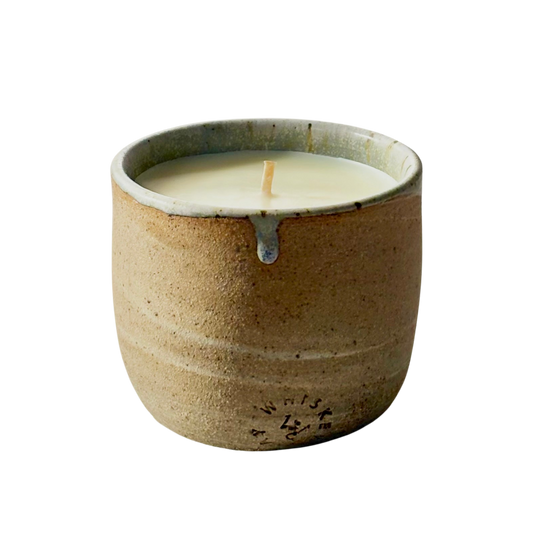 An organic candle in a handmade, speckled beige cup with a small blue-gray accent at the rim, shown on a plain white background.