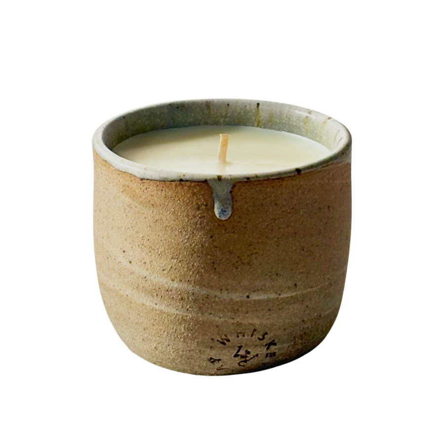 An organic candle in a handmade, speckled beige cup with a small blue-gray accent at the rim, shown on a plain white background.