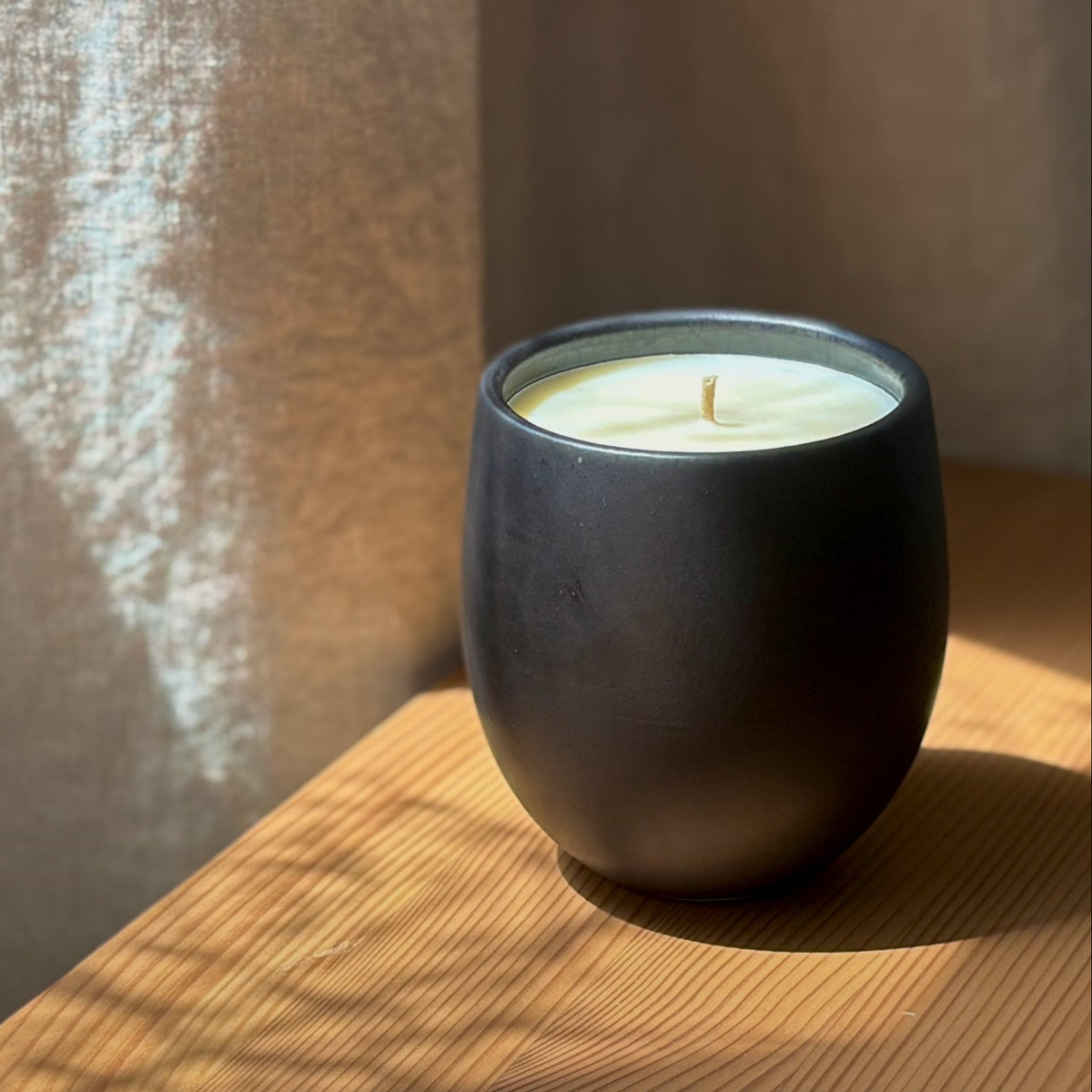 Organic candle in black ceramic vessel on a wooden surface with 'The Organic Candle Co.' branding.