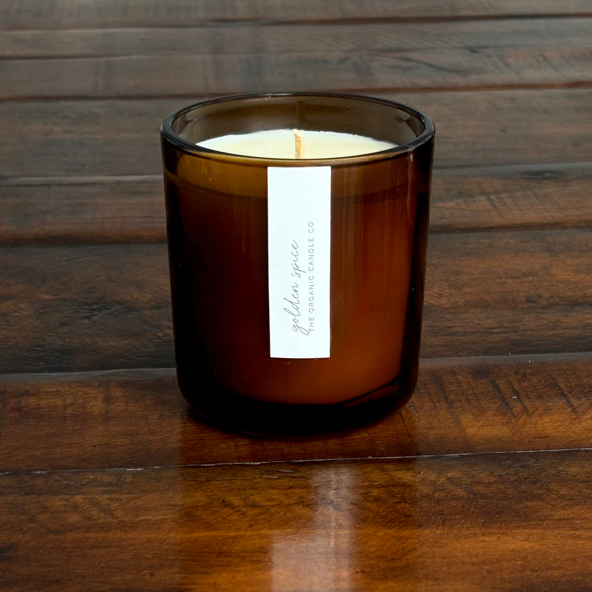 An organic candle in an amber glass jar candle with a white paper label reading 'golden spice THE ORGANIC CANDLE CO.' on a plain white background.