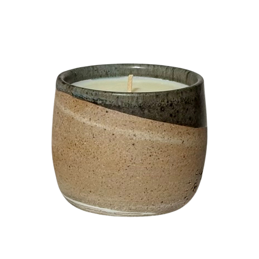 An organic candle in a hand-made stoneware cup with a diagonal split design. The lower half is a speckled warm beige, while the upper half is a dark, glossy charcoal gray.