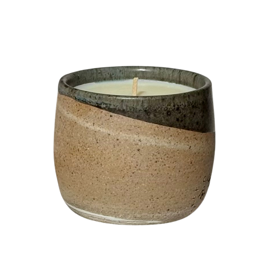 An organic candle in a hand-made stoneware cup with a diagonal split design. The lower half is a speckled warm beige, while the upper half is a dark, glossy charcoal gray.
