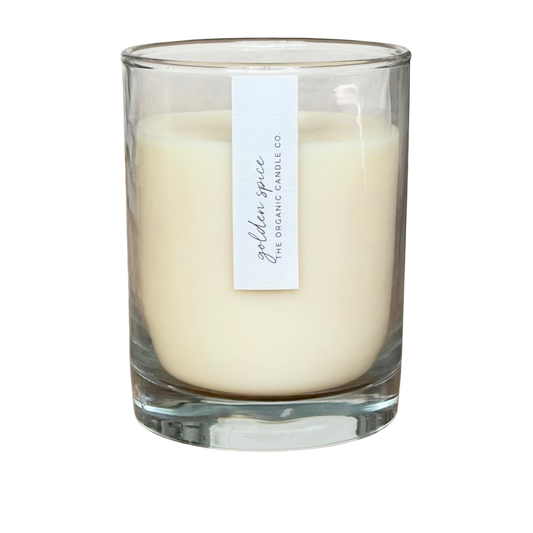 An organic candle in a clear glass jar filled, featuring a vertical white label that reads 'golden spice' and 'THE ORGANIC CANDLE CO.' on a plain white background.
