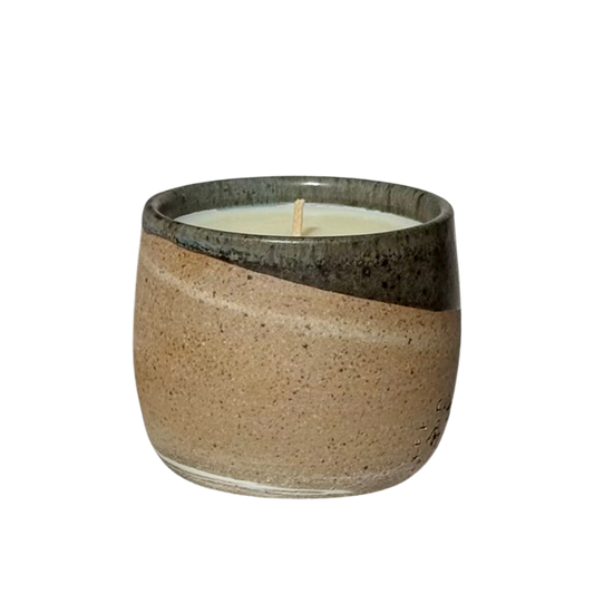 An organic candle in a hand-made stoneware cup with a diagonal split design. The lower half is a speckled warm beige, while the upper half is a dark, glossy charcoal gray.