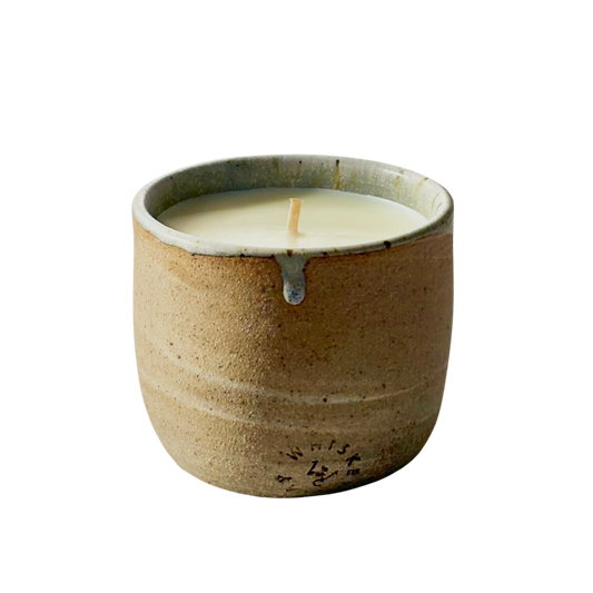 An organic candle in a handmade, speckled beige cup with a small blue-gray accent at the rim, shown on a plain white background.