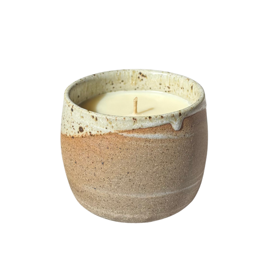 An organic candle in a handmade stoneware cup, set against a plain white background.