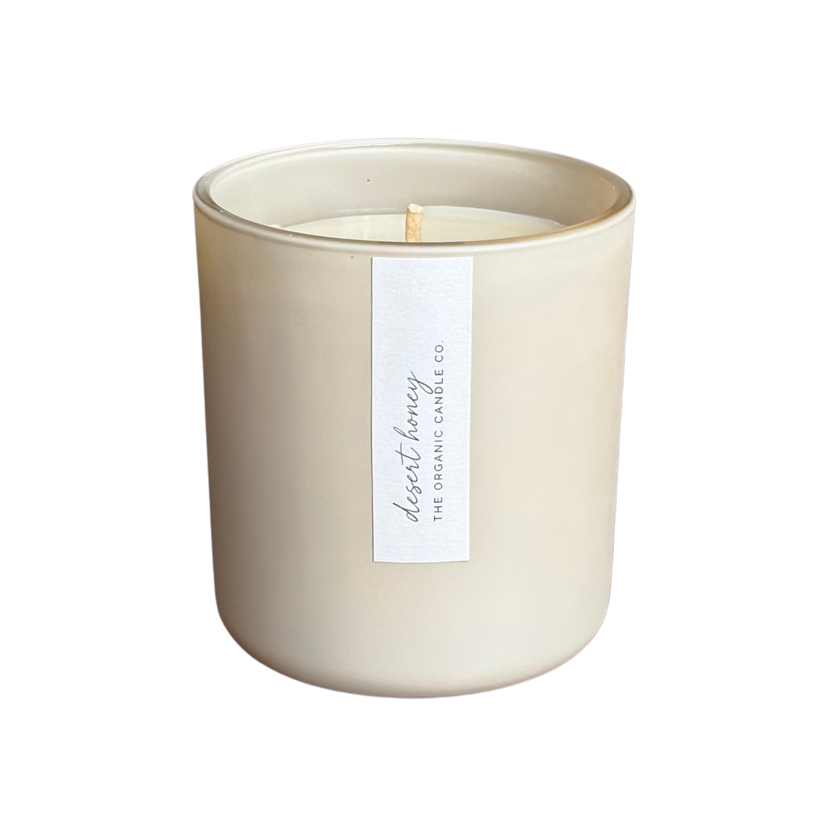 An organic candle in a matte cream-colored glass jar with a single white paper label reading 'desert honey THE ORGANIC CANDLE CO.' on a plain white background.