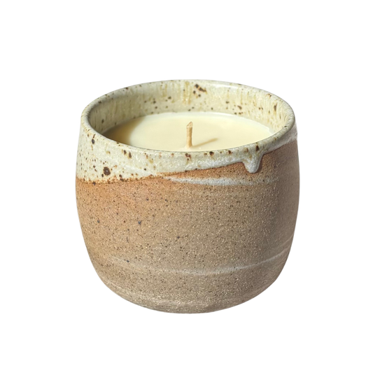 An organic candle in a handmade stoneware cup, set against a plain white background.