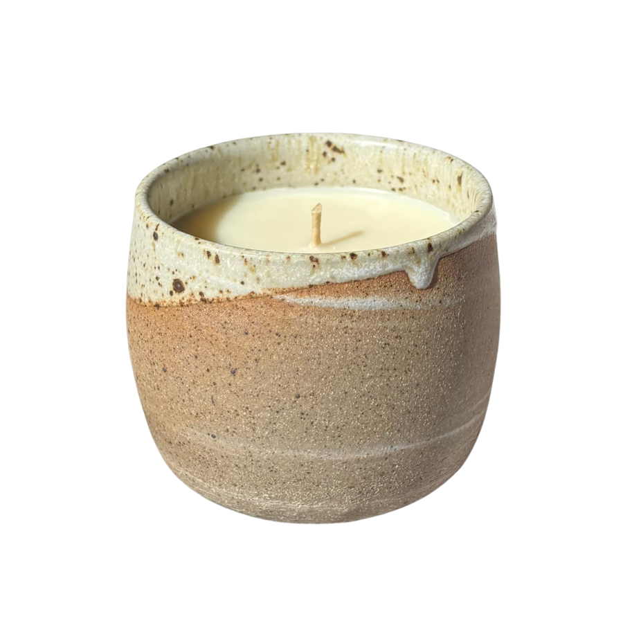 An organic candle in a handmade stoneware cup, set against a plain white background.