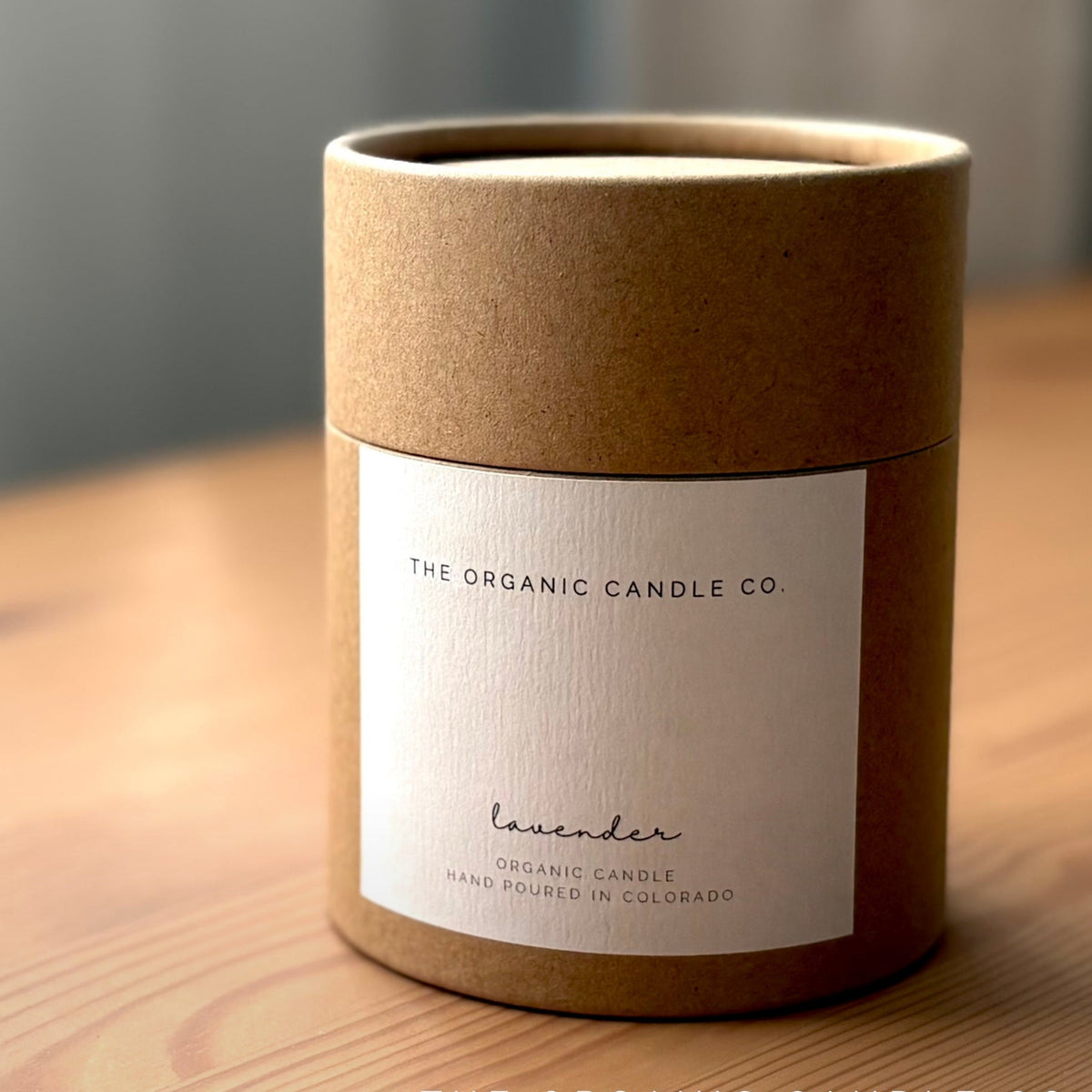 Cylindrical brown candle container with 'The Organic Candle Co' label on a wooden surface.