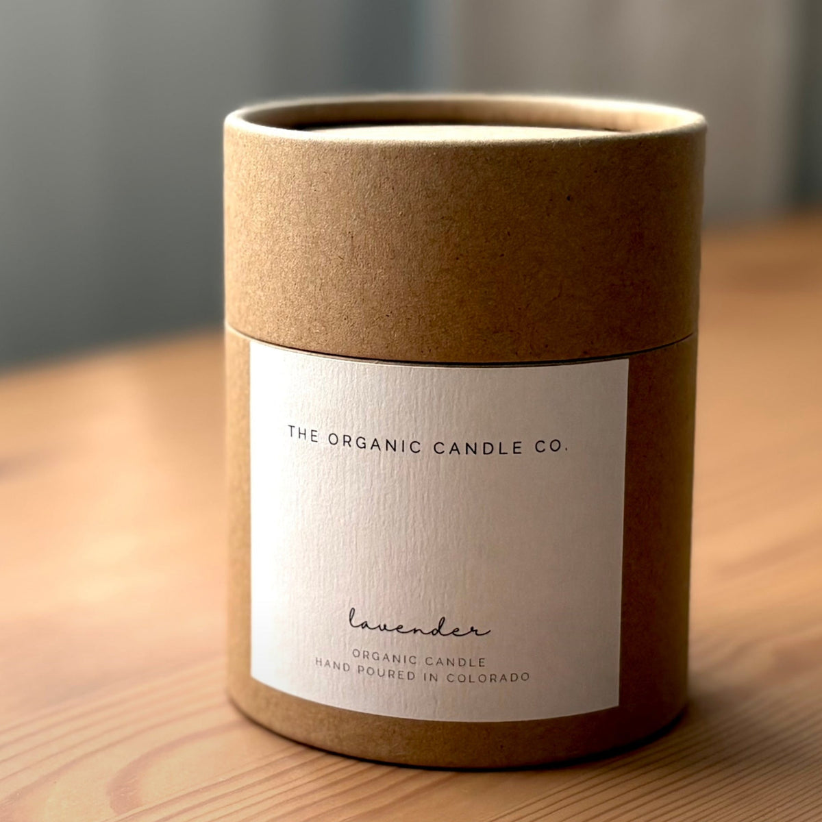 Cylindrical brown candle container with 'The Organic Candle Co' label on a wooden surface.
